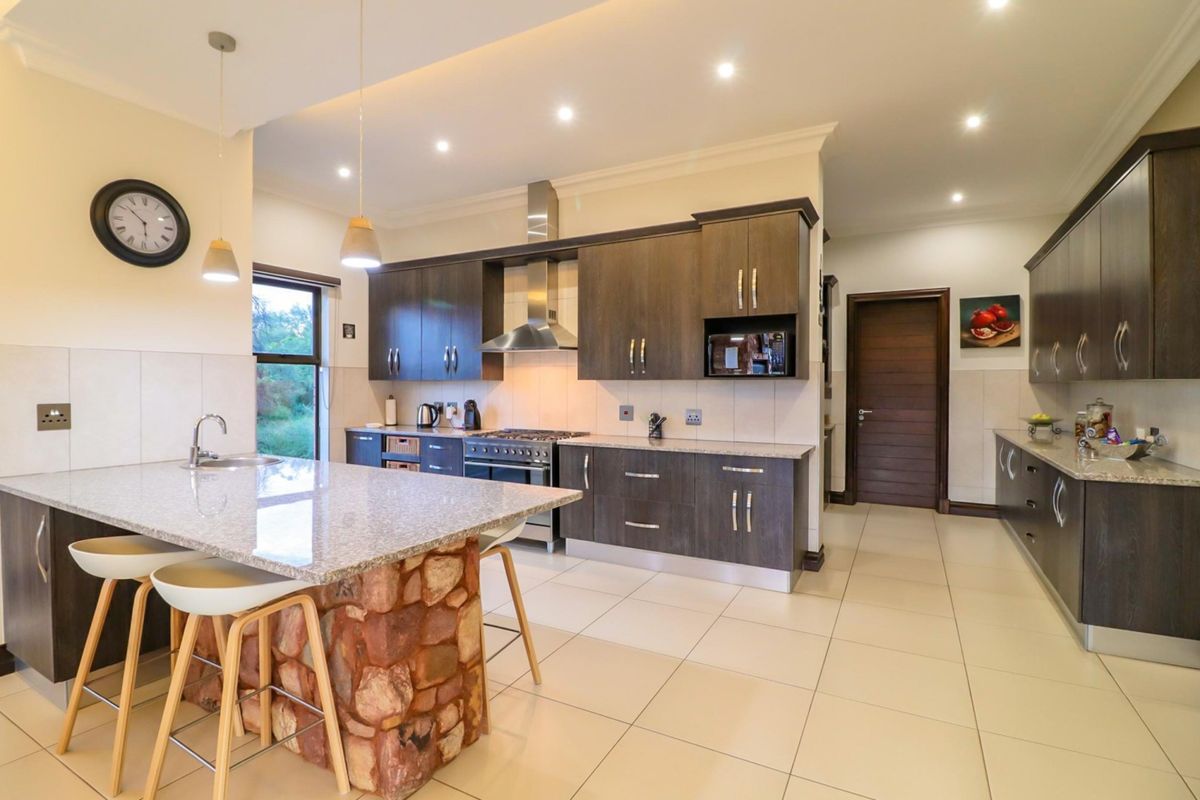 Modern kitchen featuring dark wood cabinetry, granite countertops, a stone-clad breakfast island, stainless steel appliances, and recessed ceiling lighting.