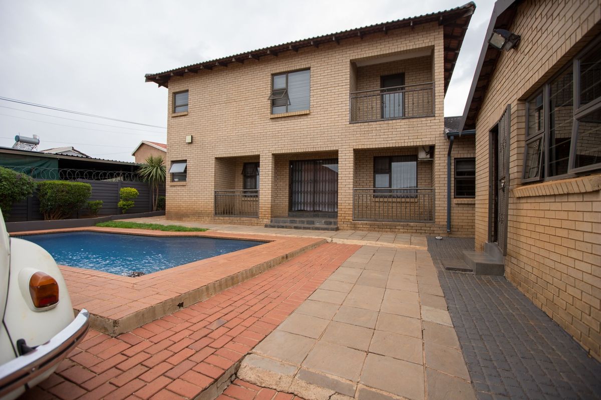 Rear view of a double-story brick house featuring a swimming pool, paved patio area, and upper-level balconies.