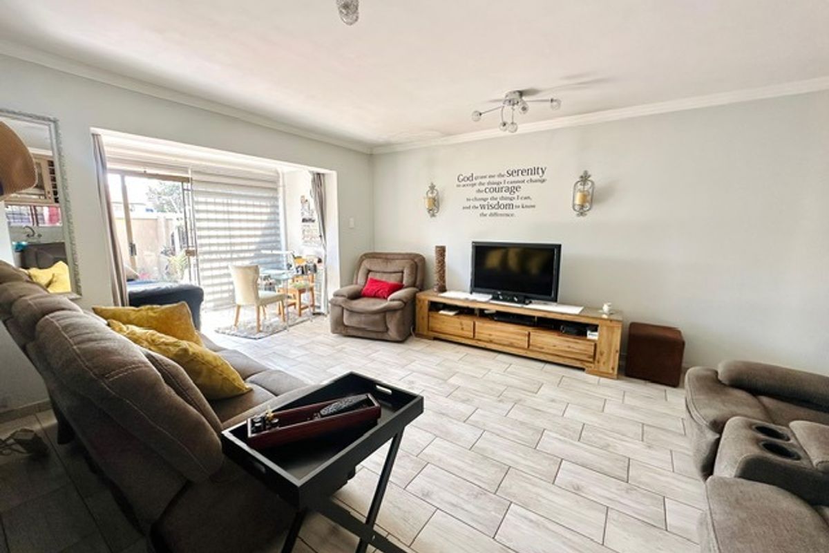 Spacious living room featuring light-toned floor tiles, recessed sliding doors leading to an outdoor area, and modern ceiling light fixtures.