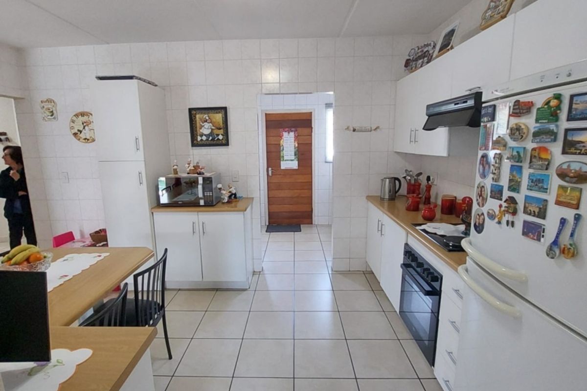 A functional kitchen featuring white cabinetry, tiled walls and flooring, a built-in oven, and a hob with an extractor fan.