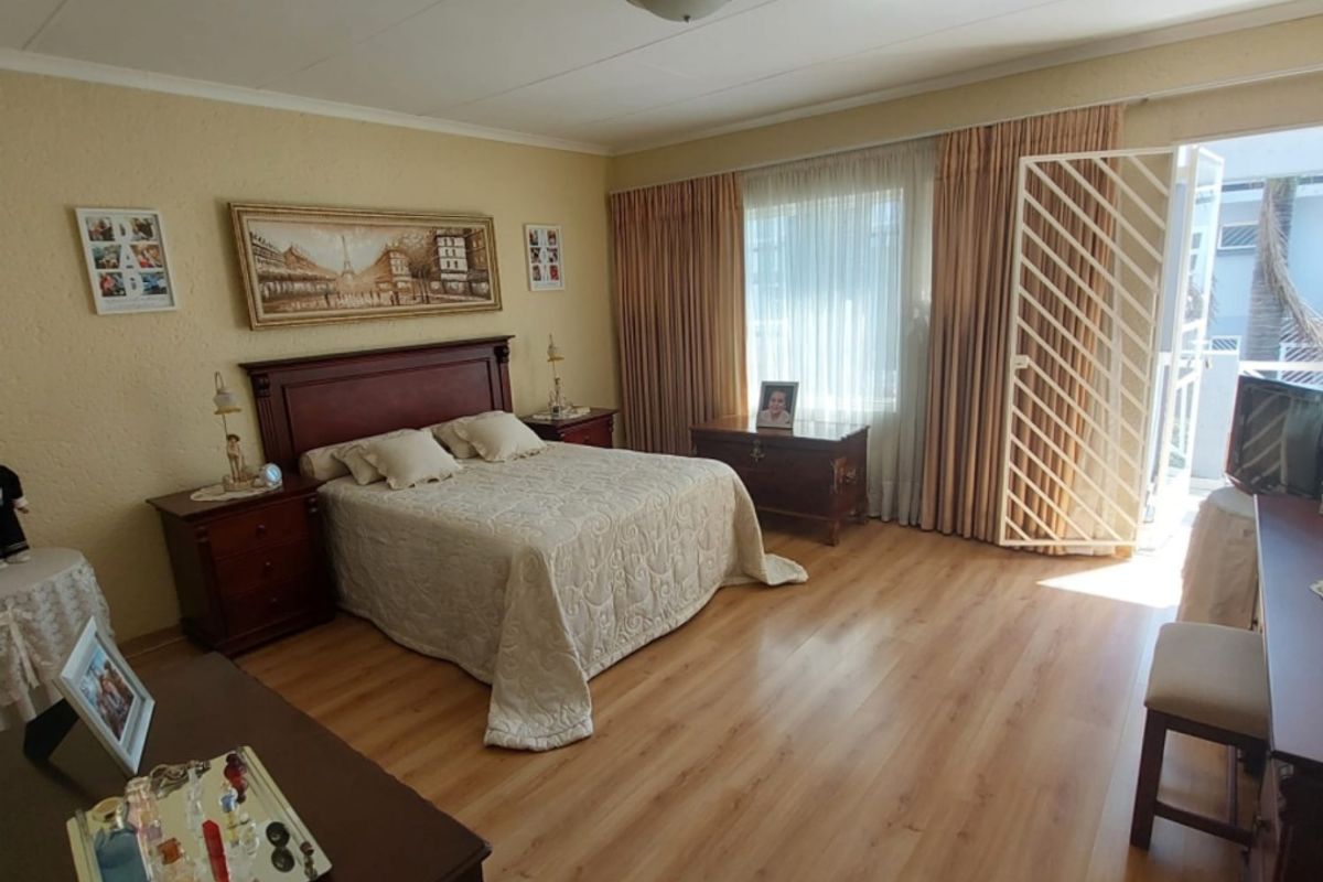 Spacious bedroom featuring wood-look laminate flooring, a ceiling-mounted light fixture, and direct access to an outdoor balcony through a security gate.