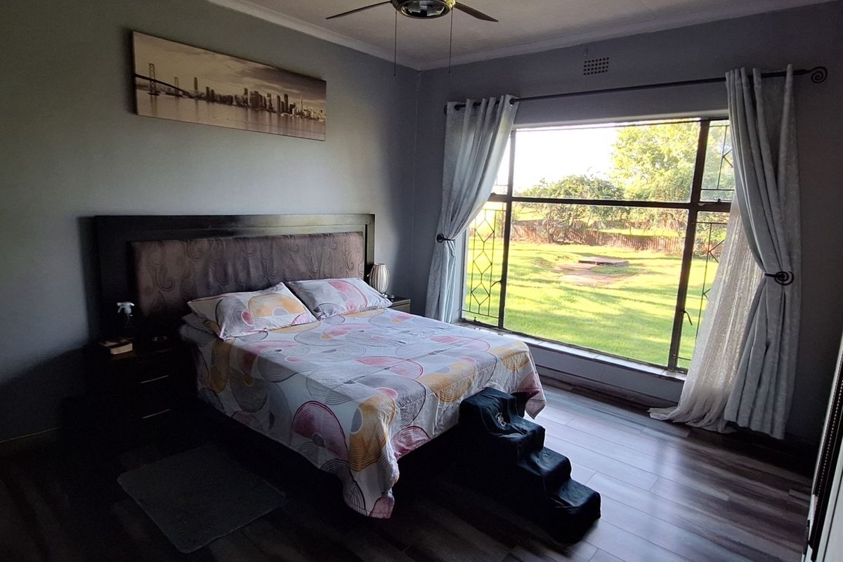 A bedroom featuring laminate flooring, a ceiling fan, and a large window providing natural light and views of the garden.