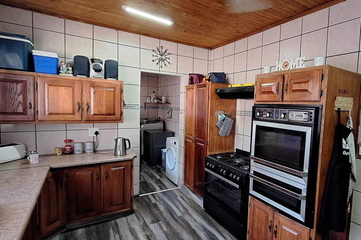 A functional kitchen featuring wooden cabinetry, built-in double oven, gas hob, and tiled wall finishes, with an adjacent scullery area visible.