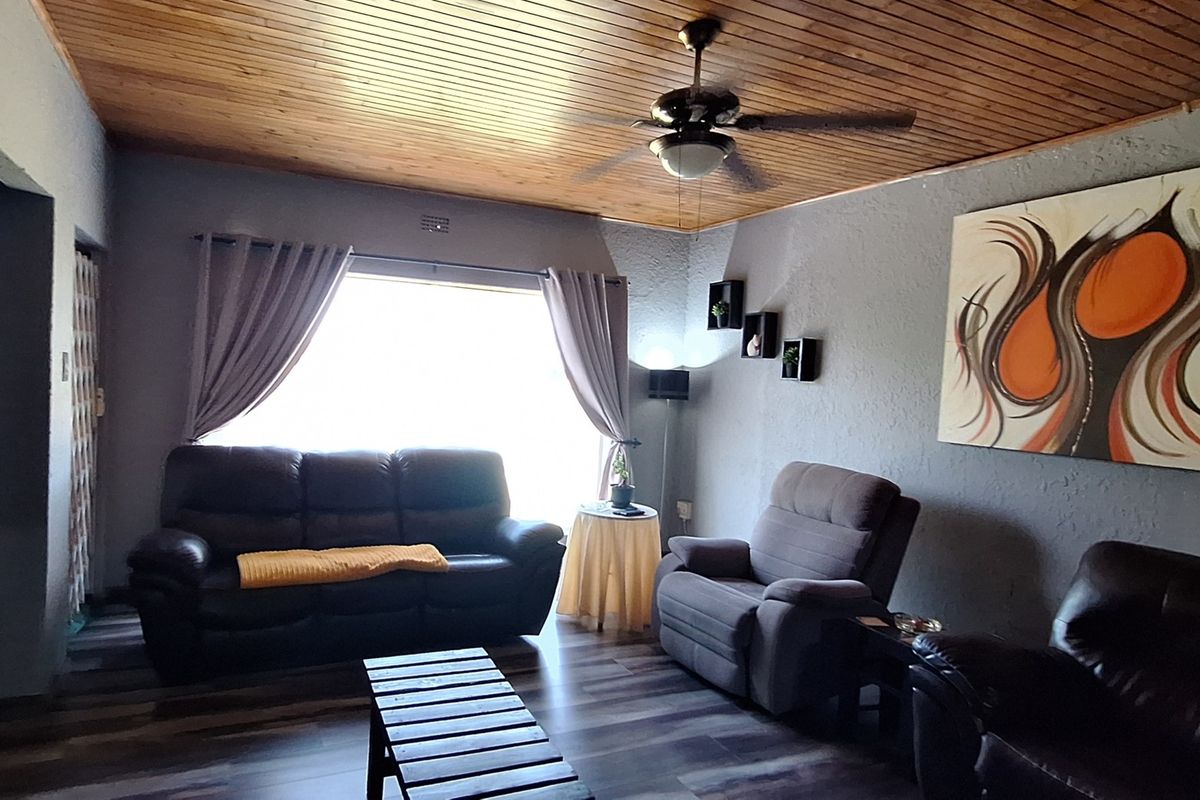 A cozy living room featuring a warm timber tongue and groove ceiling, ceiling fan, and modern laminate flooring.