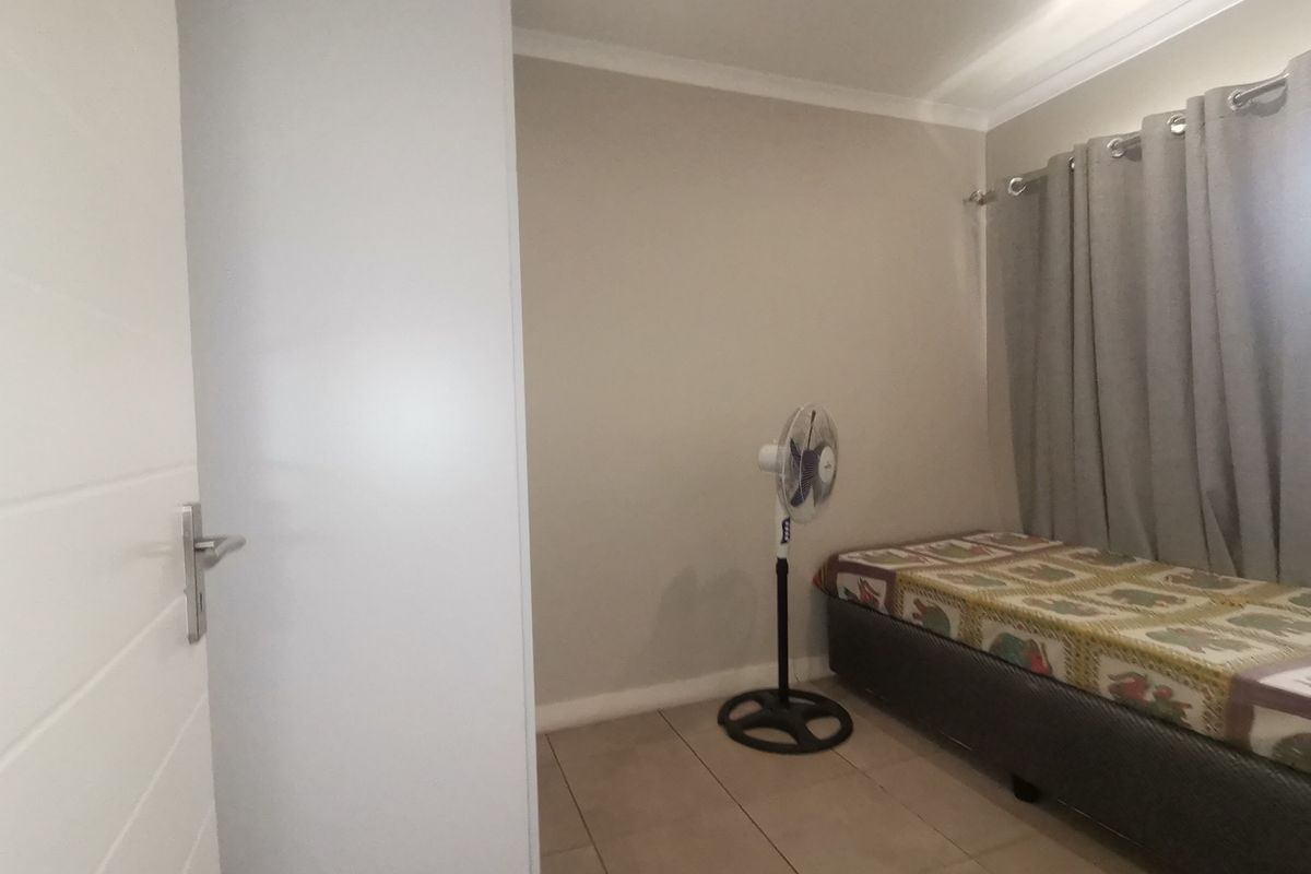 A compact bedroom featuring neutral wall tones, tiled flooring, and built-in curtain rails.