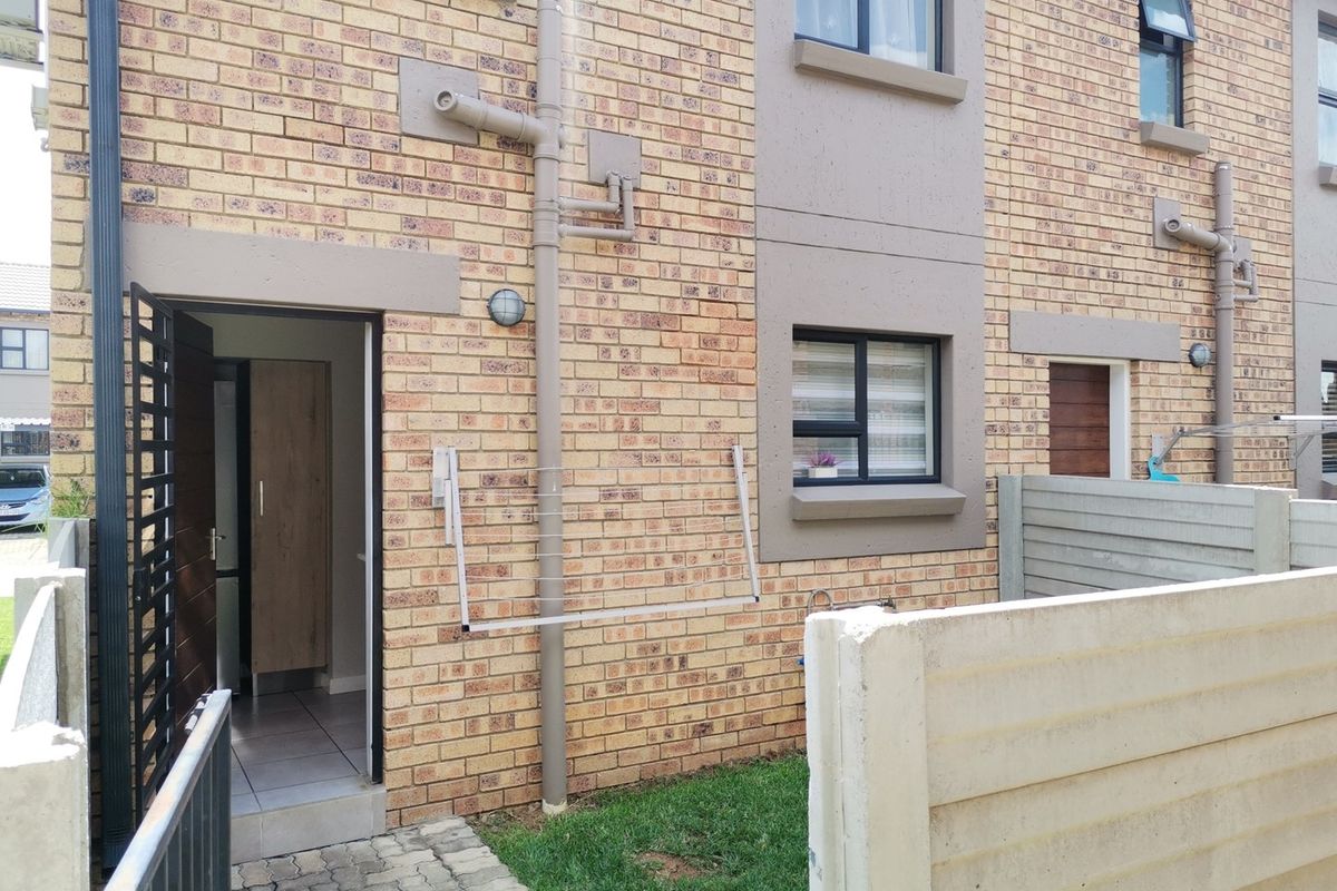 Rear exterior view of the townhouse featuring face-brick facade, paved walkway, small lawn area, and secure boundary walling.