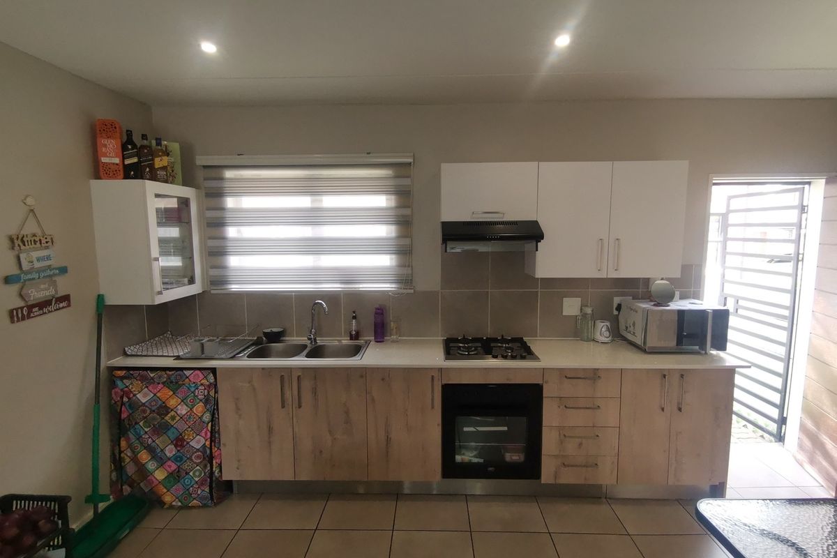 A functional kitchen featuring light wood-finish cabinetry, a built-in gas hob, an under-counter oven, an extractor fan, and a double-basin sink.