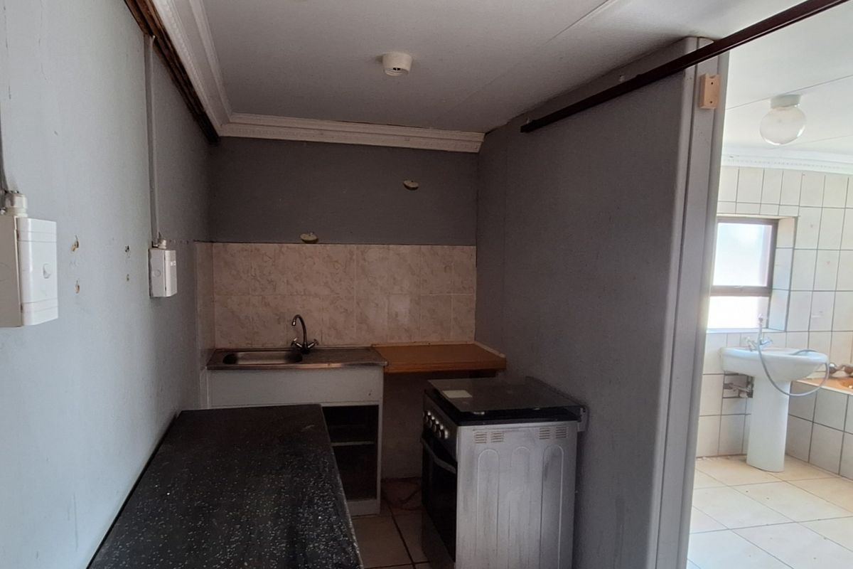 A small, basic kitchen area featuring a sink, stove, and tiled splashback, with an adjacent bathroom visible through the doorway.