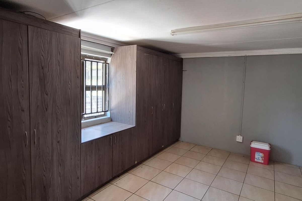 A spacious bedroom featuring extensive built-in cupboards, tiled flooring, and security bars on the window, offering a clean and functional living space.