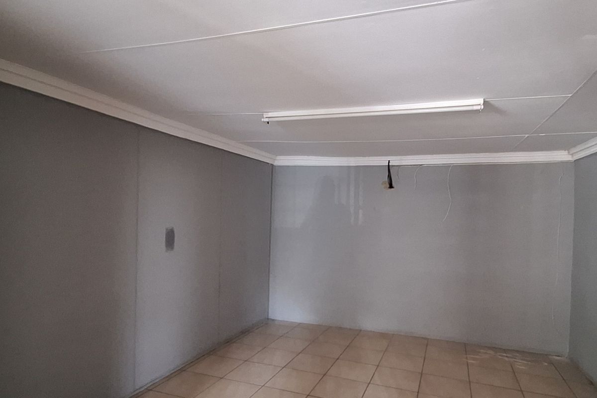 An empty living area featuring tiled flooring, ceiling cornices, and a fluorescent light fixture, currently requiring minor electrical and wall finishing repairs.