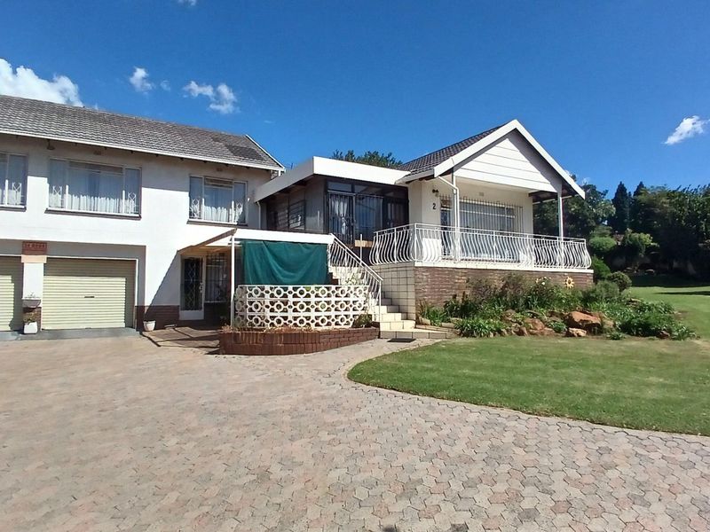 Front elevation of a multi-level house featuring a paved driveway, double garage, and an elevated covered patio with wrought iron railings.