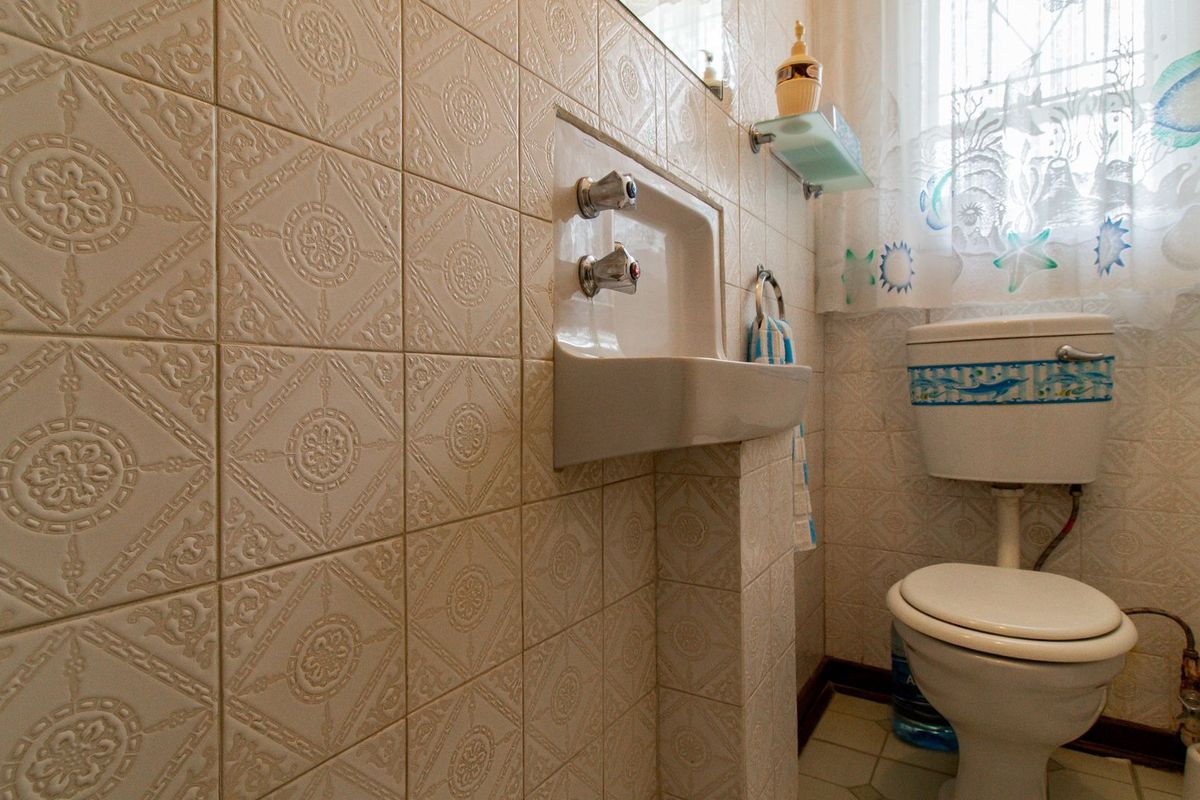 A compact bathroom featuring patterned ceramic wall tiles, a wall-mounted basin, and a standard toilet.