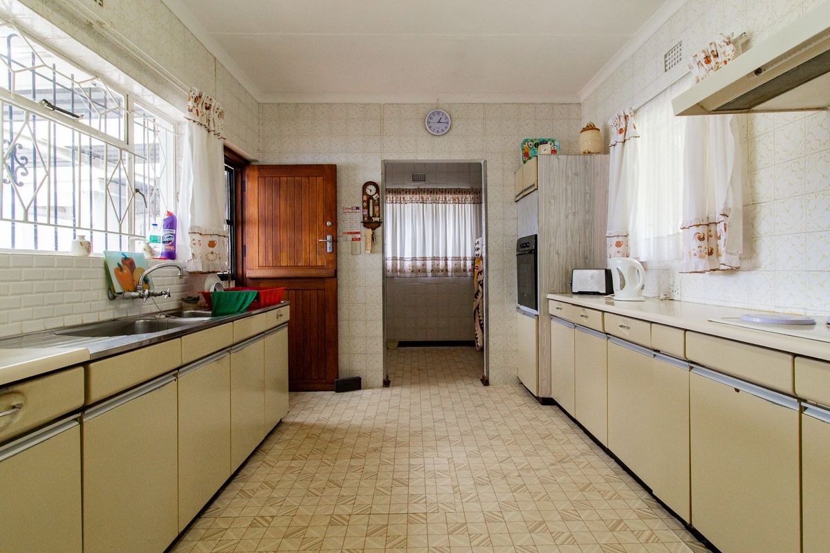 A functional, dated kitchen featuring original cabinetry, built-in oven, extractor fan, and tiled finishes, offering significant potential for a modern renovation.