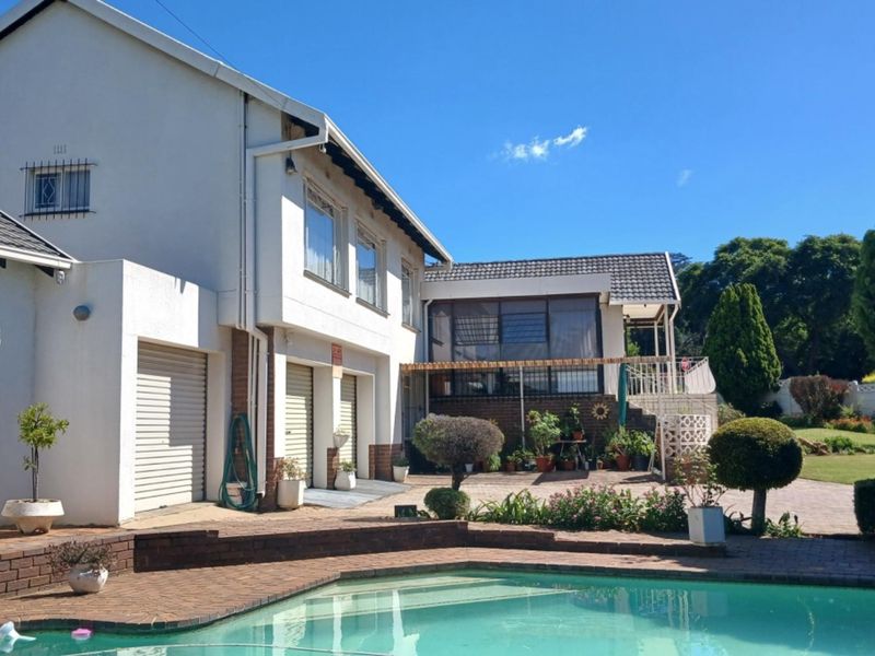 Rear view of the property featuring a swimming pool, brick paved patio area, and multi-level building structure with garage access.
