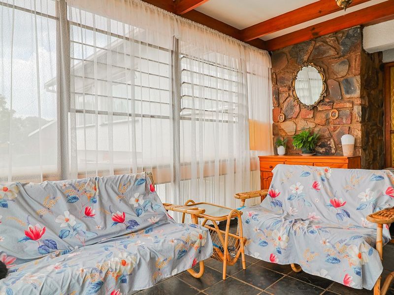 Enclosed patio area featuring a rustic stone feature wall, exposed timber ceiling beams, and durable slate tile flooring with large louvre windows.