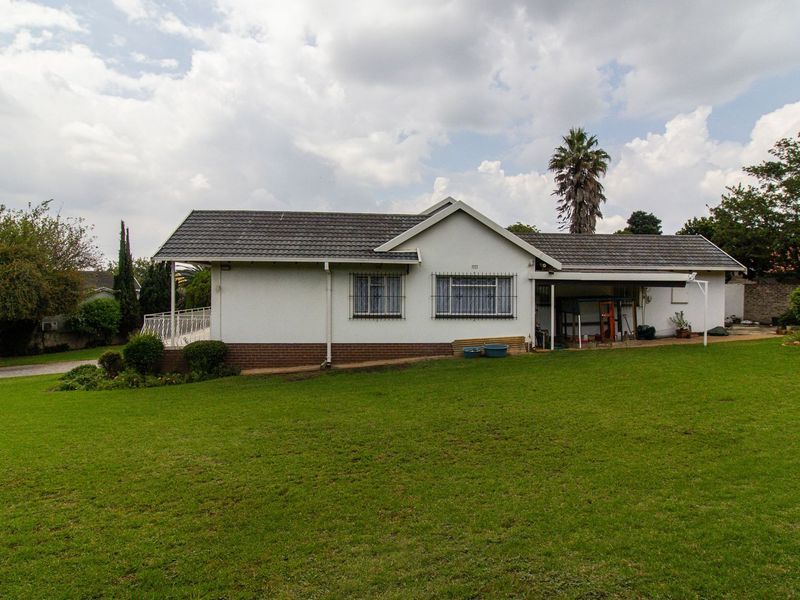 A rear view of a single-story house featuring a tiled roof, brick base, and a covered patio area overlooking a spacious lawn.