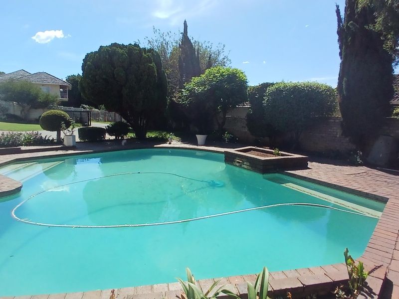 Outdoor swimming pool area featuring brick paving, established garden landscaping, and a brick boundary wall.