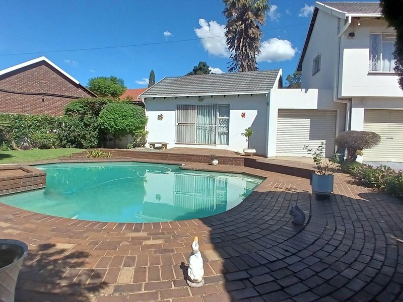 A backyard area featuring a swimming pool with brick paving, adjacent to a garage and a residential building structure.
