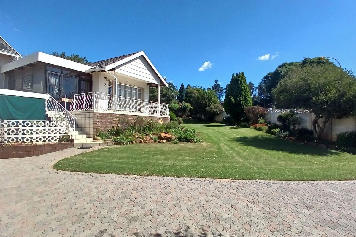 Spacious rear exterior view featuring a paved driveway, elevated patio with metal balustrades, and a well-maintained landscaped garden.