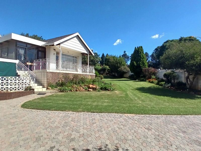 Spacious rear exterior view featuring a paved driveway, elevated patio with metal balustrades, and a well-maintained landscaped garden.