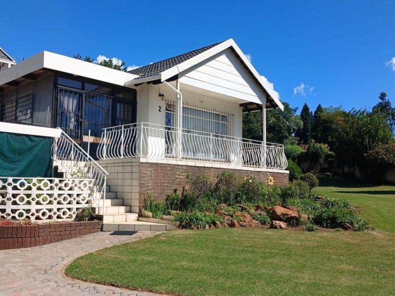 A well-maintained front elevation featuring a raised tiled patio with wrought iron balustrades, brick accents, and a spacious landscaped garden.