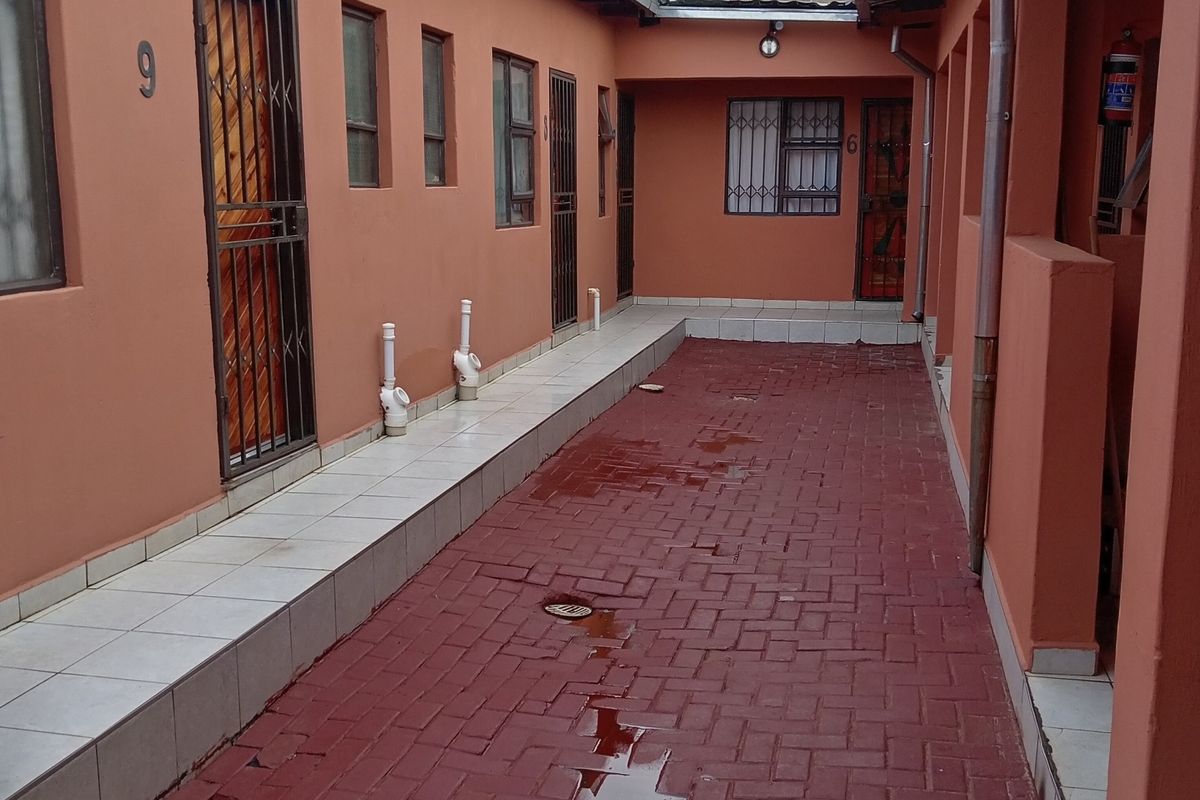 Exterior view of a residential complex corridor featuring paved walkways, security gates, and access to multiple units.