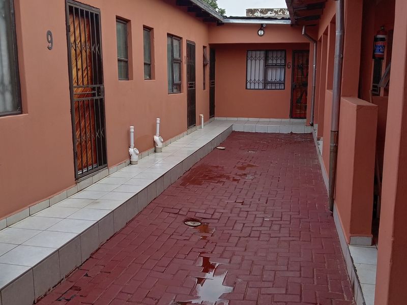 Exterior view of a residential complex corridor featuring paved walkways, security gates, and access to multiple units.
