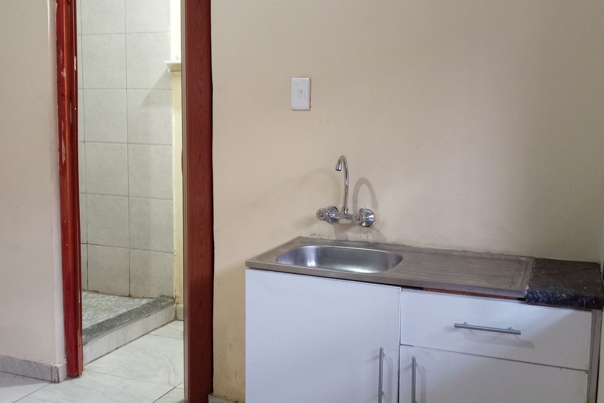 A compact kitchenette area featuring a single stainless steel sink, base cabinetry, and tiled flooring, with an adjacent doorway leading to a tiled bathroom.