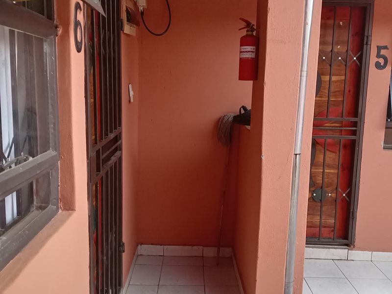 A covered outdoor walkway or patio area featuring tiled flooring, security gates, and external building infrastructure.