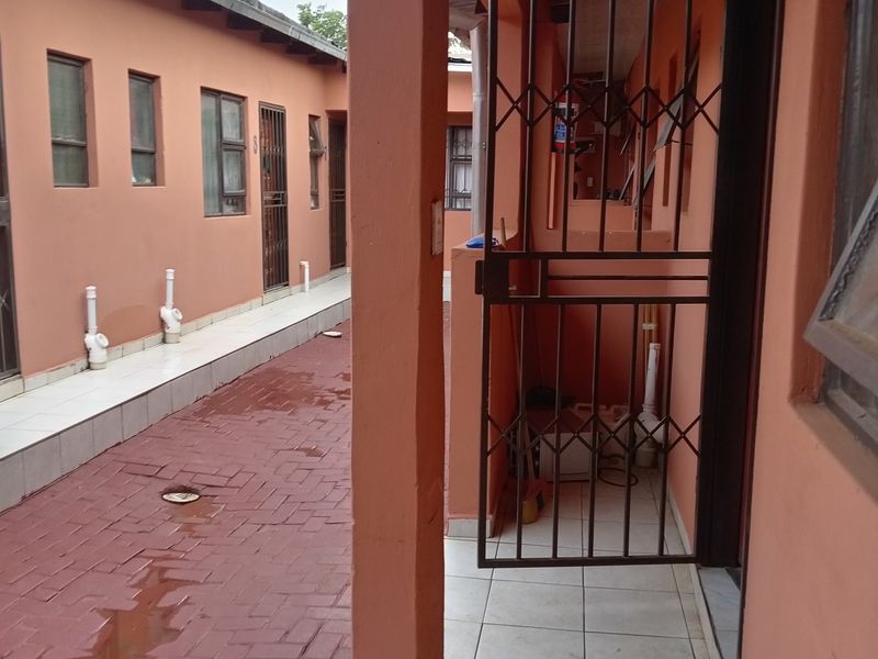 A narrow exterior walkway featuring paved flooring, tiled patio sections, and security gates, providing access to multiple residential units.