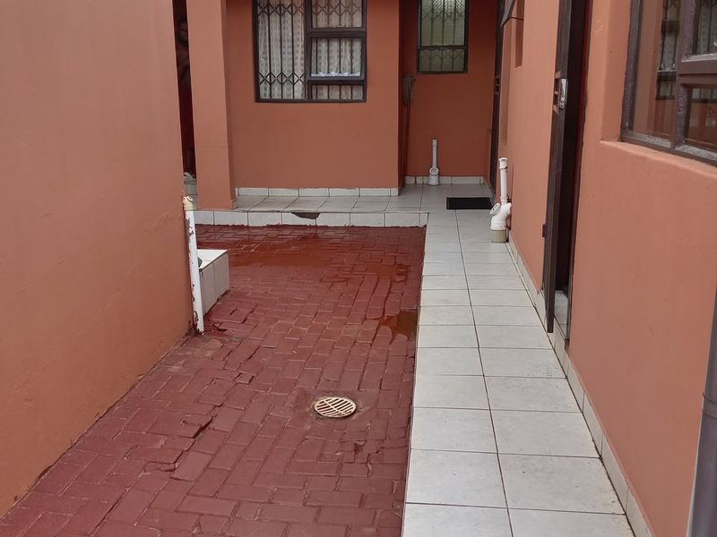 A rear exterior courtyard area featuring a combination of red brick paving and a tiled walkway with external drainage and security window bars.