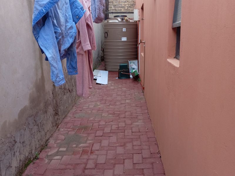 A narrow side passage featuring paved flooring, a water storage tank, and boundary walls.