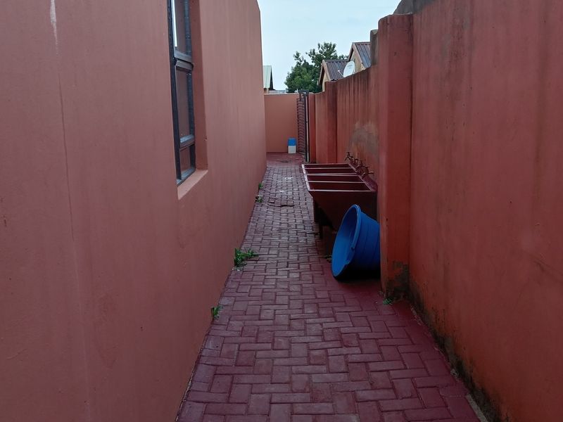 A narrow side passage featuring red paved flooring, boundary walls, and fixed external wash troughs.