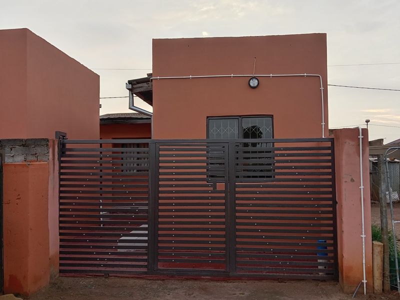 Front view of a residential property featuring a metal security gate, perimeter wall, and security bars on the window.