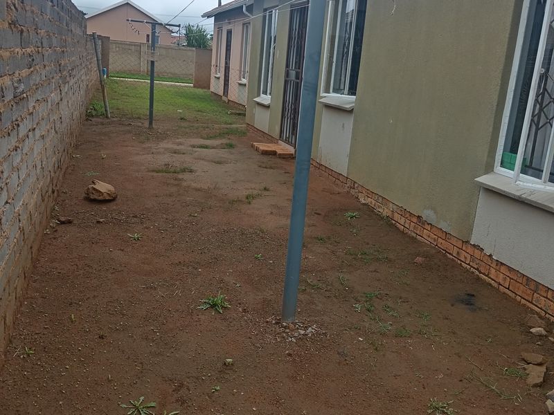 Rear exterior view of the property featuring a large dirt yard, brick boundary wall, and fixed metal washing lines.