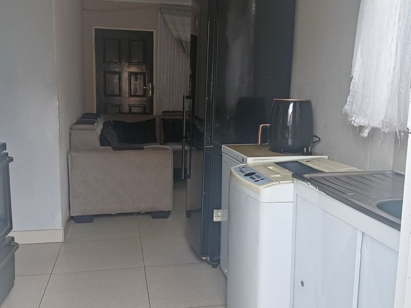 An open-plan living and kitchen area featuring tiled flooring, basic cabinetry, and a sink, with visible signs of wear on the walls and ceiling.