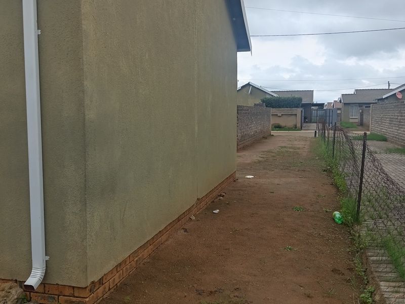 A view of the side and rear exterior area of the house, featuring a plain rendered wall, downpipe, and basic wire fencing.