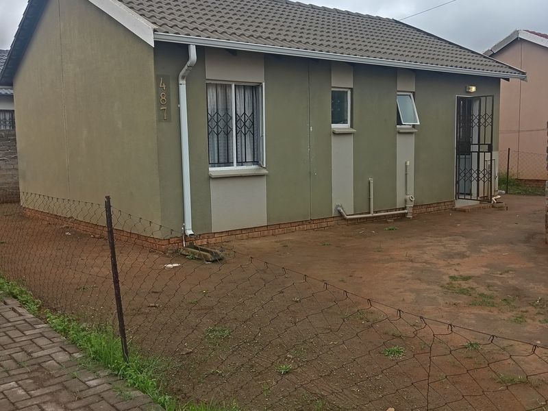 A single-story residential house featuring a tiled roof, security gates, and security bars on windows, situated on an unpaved plot.