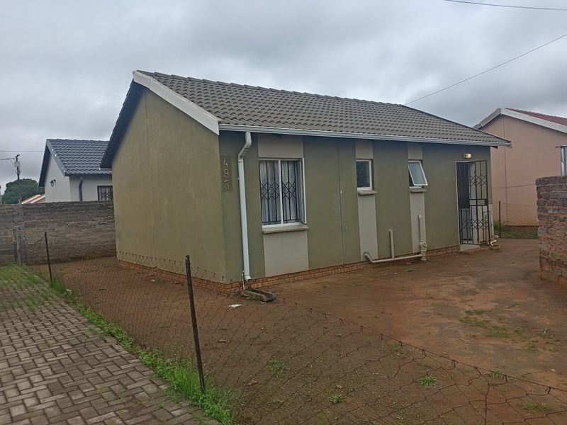 A detached single-story house featuring a tiled roof, security gates, and an unpaved yard area enclosed by wire fencing and brick walls.