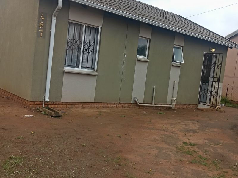 Front elevation of a single-story house featuring a tiled roof, security gates, and security bars on windows, set on an unpaved plot.