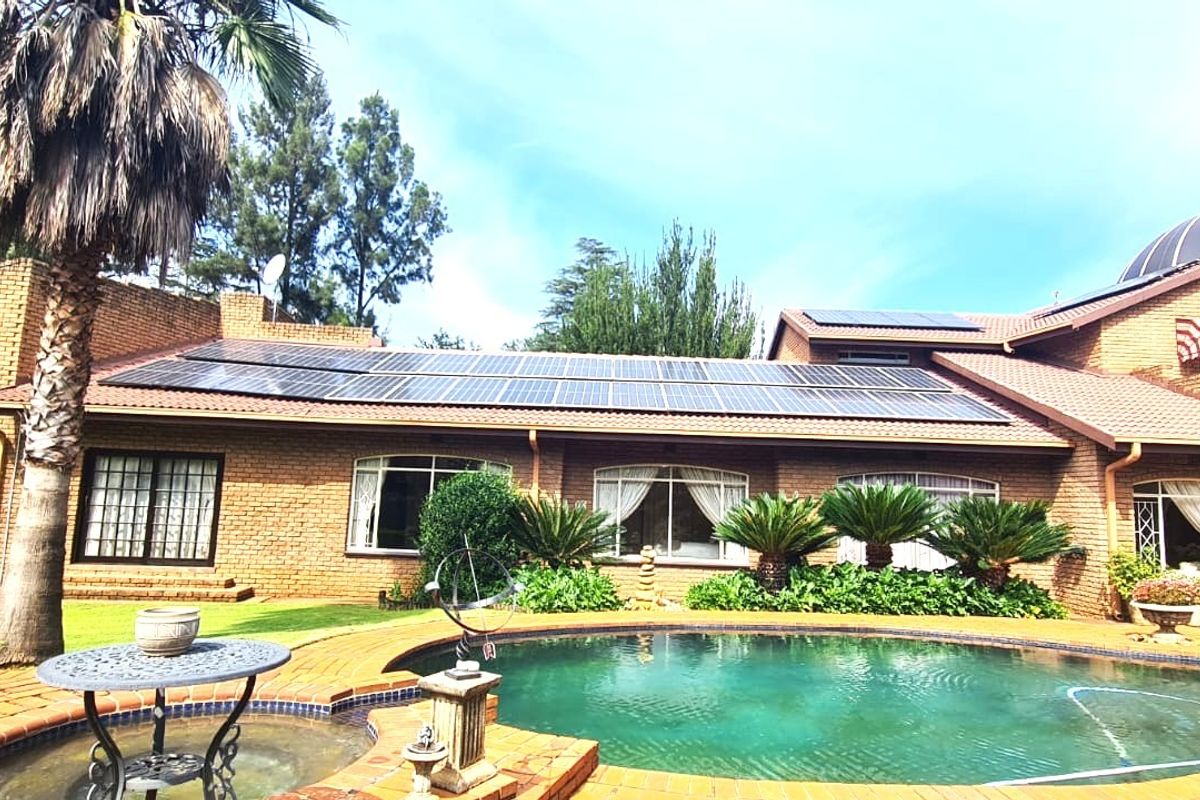 Rear view of a brick house featuring a swimming pool, extensive solar panel installation on the roof, and a distinctive dome architectural element.