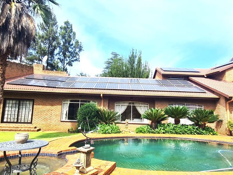 Rear view of a brick house featuring a swimming pool, extensive solar panel installation on the roof, and a distinctive dome architectural element.