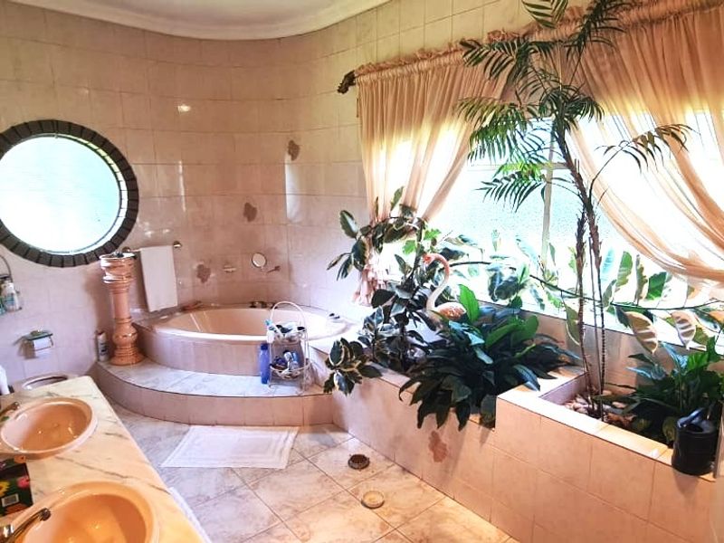 Spacious bathroom featuring a sunken bathtub, double vanity, and a unique porthole window, requiring cosmetic updates to modernize the dated tile finishes.