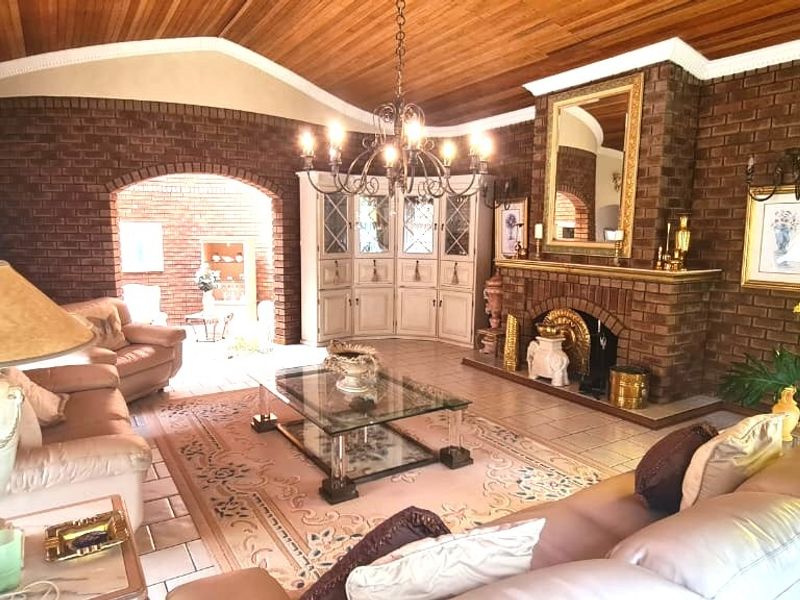 Spacious living room featuring a prominent brick fireplace, warm timber ceiling, tiled flooring, and a unique circular window, offering a classic, character-filled aesthetic.