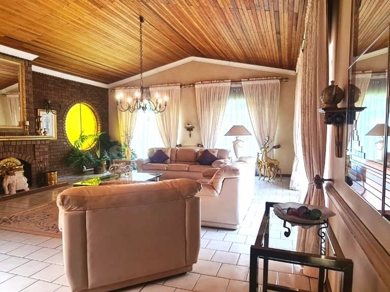 Spacious living room featuring a prominent brick fireplace, vaulted timber-clad ceiling, tiled flooring, and decorative mirrored wall paneling.