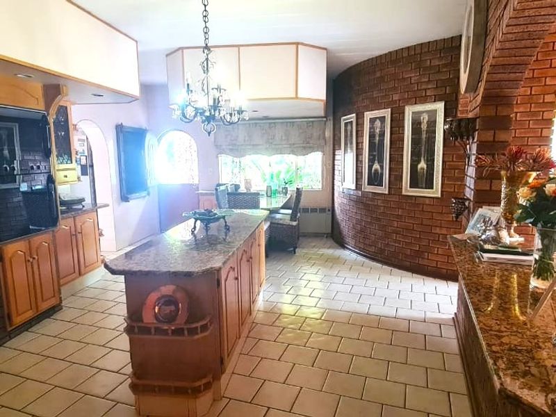 Spacious open-plan kitchen and dining area featuring granite countertops, custom cabinetry, a central island, and distinctive exposed brick walls.