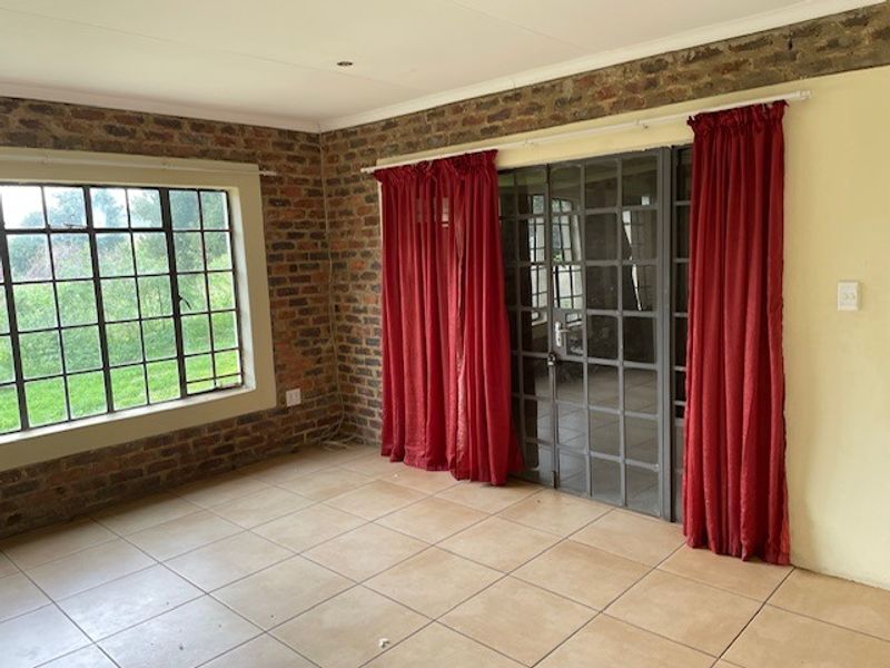 Spacious living area featuring exposed brick walls, tiled flooring, and large steel-framed windows providing natural light and garden views.