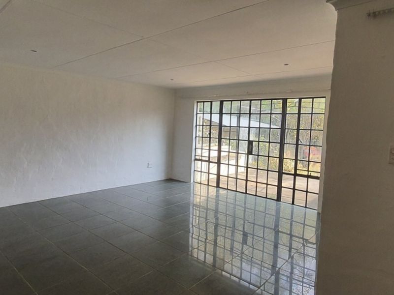 A spacious, empty living area featuring dark tiled flooring, recessed ceiling lights, and a large glass sliding door providing access to the exterior.