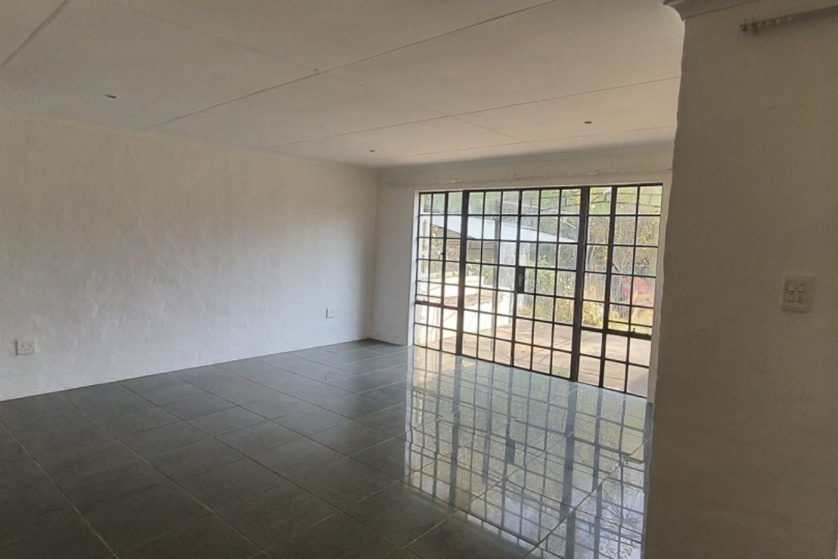 A spacious, empty living area featuring dark tiled flooring, recessed ceiling lights, and a large glass sliding door providing access to the exterior.