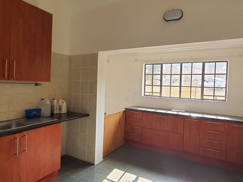 A functional kitchen featuring wooden cabinetry, dark countertops, a gas hob with extractor fan, and a double basin sink with tiled backsplash.